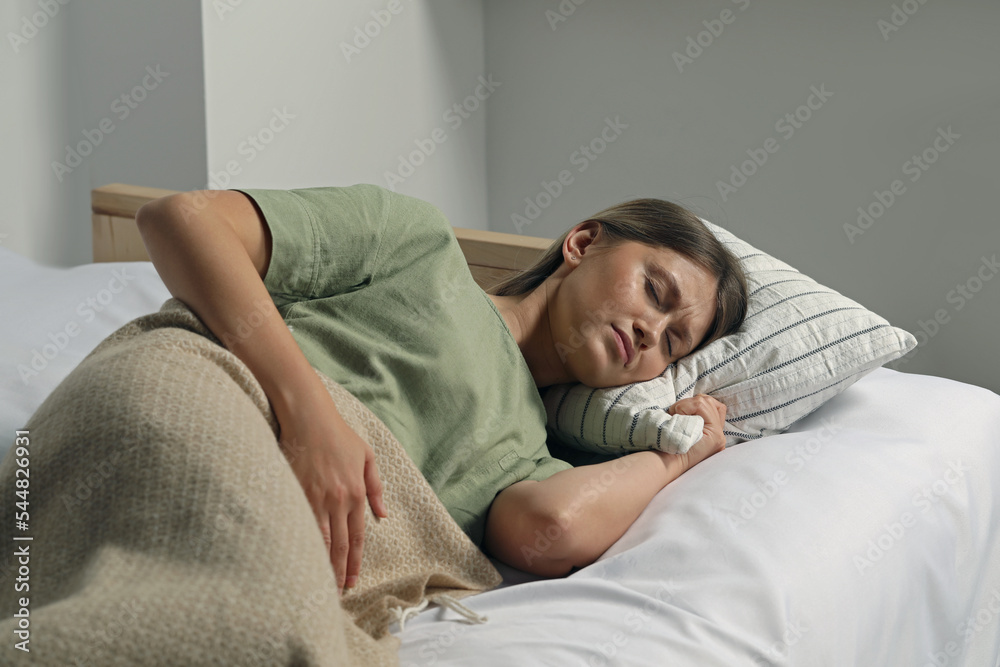 Sticker Young woman suffering from menstrual pain in bed at home