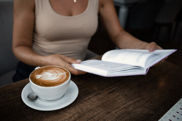 Unrecognizable woman sits at table in cafe with cup of coffee and reads a book 