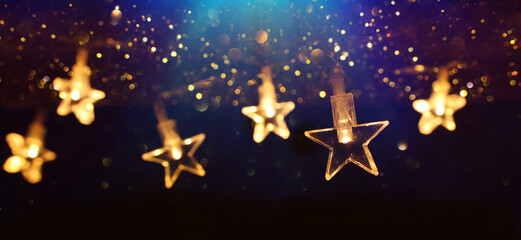 Christmas warm gold garland lights over dark background with glitter overlay - obrazy, fototapety, plakaty