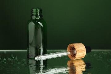 Bottle of face serum and dropper on wet surface against green background, closeup