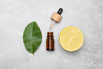 Bottle of essential oil with lemon slice and leaf on grey table, flat lay