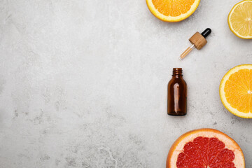 Bottle of citrus essential oil and fresh fruits on light table, flat lay. Space for text