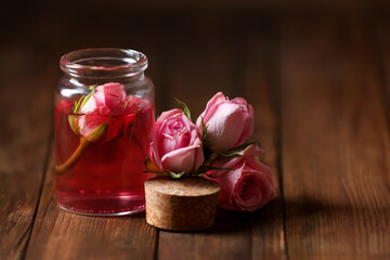 Bottle of essential rose oil and flowers on wooden table