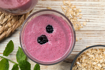 Glass of blackberry smoothie with mint and oatmeal on light wooden table, flat lay