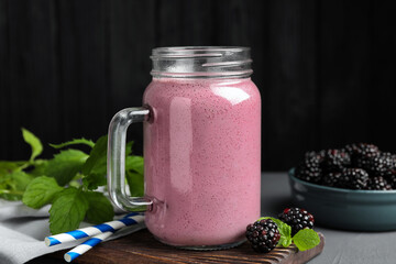 Mason jar of blackberry smoothie, mint and berries on grey table