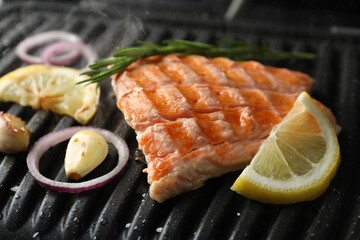 Tasty salmon cooking with rosemary, garlic, onion and lemon on electric grill, closeup