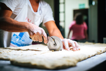 Hands full of flour, cutting dough with dough cutter roller. Homemade bread. Shop locally. Traditional preparation. Handmade. Natural, organic food. Wheel dough cutter. Bakery. Hand holding cutter.