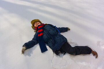 Fototapeta na wymiar A boy lies in the snow and smiles. A child plays outside in winter