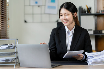 Obraz na płótnie Canvas young asian woman working with piles of financial graph chart documents Planning and analyzing marketing data with a laptop on your desk. Company business information office