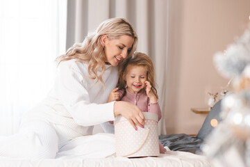 Happy smiling woman open Christmas presents in bed with little kid girl with xmas tree decorations in room at home. Winter holiday season. Motherhood.