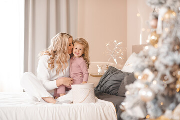 Happy smiling woman open Christmas presents in bed with little kid girl with xmas tree decorations in room at home. Winter holiday season. Motherhood.