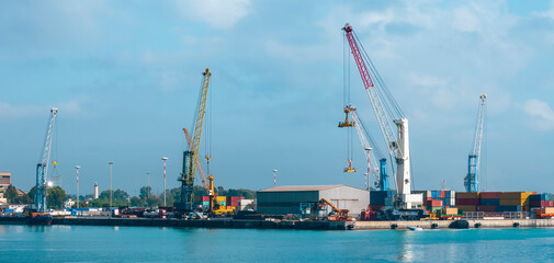 Fototapeta premium cargo sea port with cranes, container stacks and trucks with goods, sea hub terminal from seashore