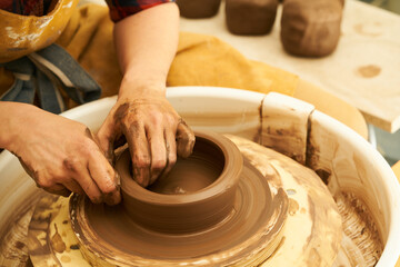 A Potter works with red clay on a Potter's wheel in the workshop..Women's hands create a pot. Girl sculpts in clay pot closeup. Modeling clay close-up. 