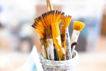 Dirty artificial bristle brushes are in a glass. Brushes after use, painting. Children's drawing...
