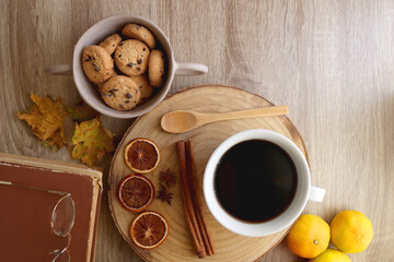 Cup of tea or coffee, seasonal spices, bowl of cookies, blanket, pumpkins, colorful leaves, books and tangerines on wooden table. Cozy hygge at home. Top view.