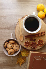 Cup of tea or coffee, seasonal spices, bowl of cookies, blanket, pumpkins, colorful leaves, books and tangerines on wooden table. Cozy hygge at home. Top view.