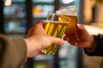 Two friends hands clinking glasses of craft beer at the pub or bar