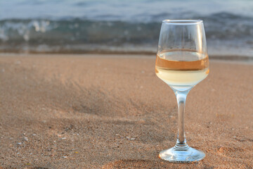 Glass of tasty wine on sand near sea, space for text
