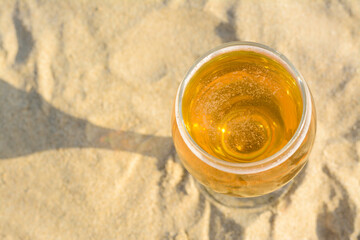 Above view of glass with cold beer on sandy beach. Space for text