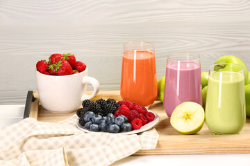 Glasses of different tasty smoothies and fresh ingredients on white wooden table