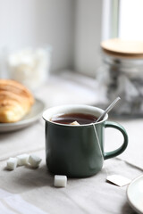 Cup of freshly brewed tea and sugar cubes on table