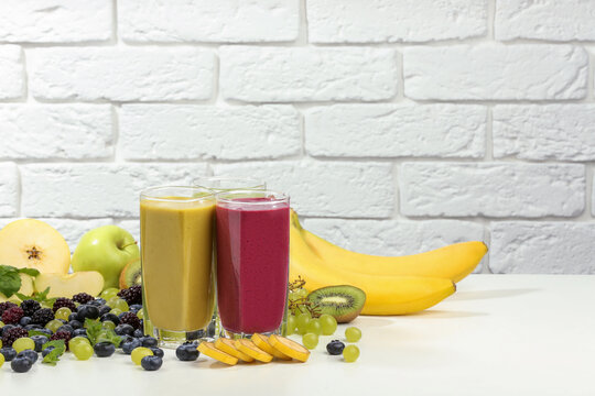 Fresh colorful fruit smoothies and ingredients on table against white brick wall. Space for text