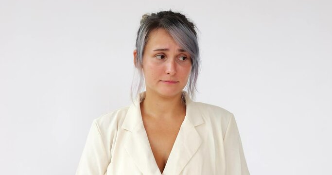 Ashamed and guilty young woman looks aside, listens to the accusations and worries. Portrait of Caucasian girl with dyed hair on white background.