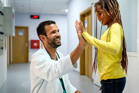 Happy little girl and paediatrician doing high five after medical checkup in hospital