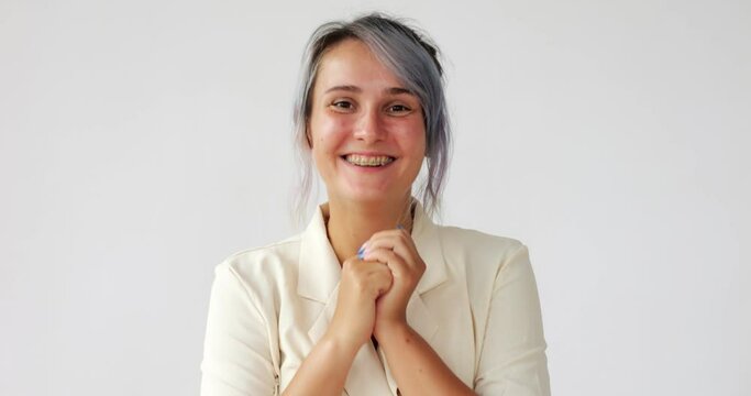 Woman is excited about something or a gift, clapping her hands cheerfully, looking straight at the camera. Portrait shot of an enthusiastic young woman, she wears corrective braces on her teeth