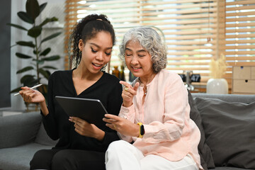 Smiling young woman teaching interested elderly mother how to use a tablet or shows some application. Elderly, technology concept