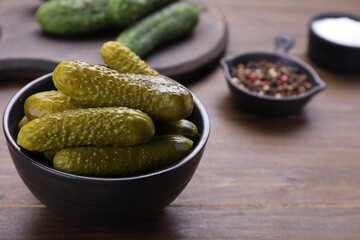 Bowl of pickled cucumbers and ingredients on wooden table, closeup