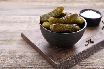 Bowl with pickled cucumbers and spices on wooden table, space for text