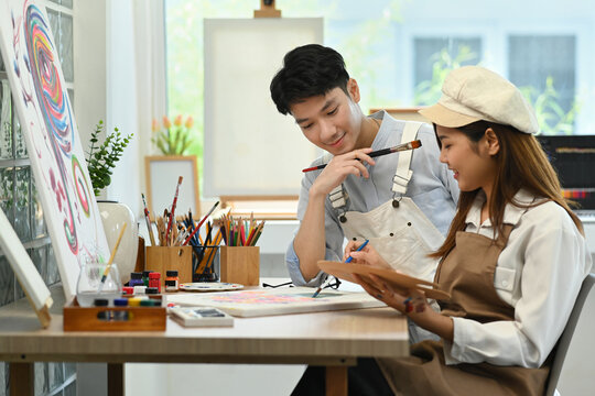 Young asian male artist and his girlfriend painting together at bright cozy art studio. Leisure activity and art concept