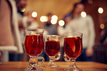 Glass cups of winter mulled wine with spices and orange slices on wooden table with Christmas decorations. Still life with traditional drink
