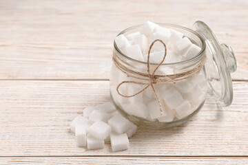 Glass jar of refined sugar cubes on light wooden table