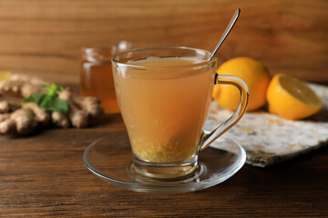 Cup of delicious ginger tea and ingredients on wooden table