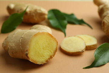 Fresh ginger and green leaves on light pale brown background, closeup