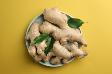 Fototapeta premium Fresh ginger with green leaves on pale light yellow background, top view