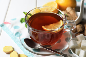 Cup of delicious ginger tea, sugar cubes and lemons on white wooden table, closeup