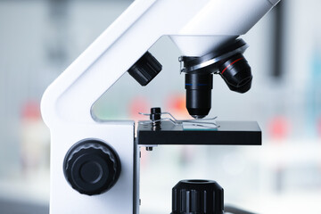 Modern medical microscope with glass slide on blurred background, closeup
