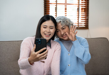 Cheerful mother and daughter using smartphone on sofa.