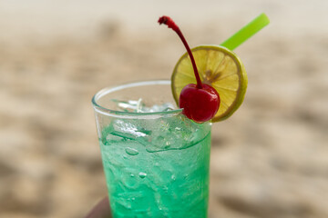 Close-up image of a green colored alcoholic cocktail drink with a cherry and a slice of citrus lemon.
