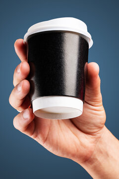 Male hand holds, raised black paper cup of tea or coffee.
