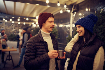 Happy couple in love in romantic dating with hot drinks, enjoying themselves, dressing warmly, looking at each other and smiling.