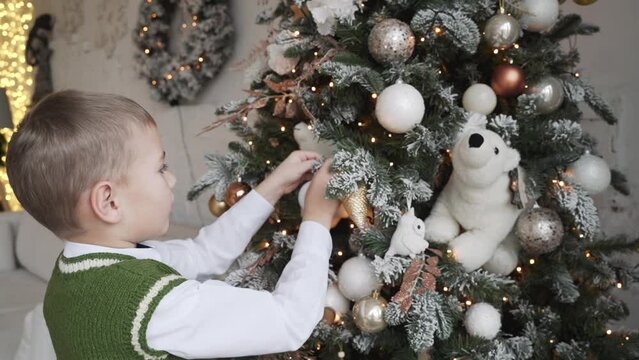 Happy little boy decorating Christmas tree with balls. 