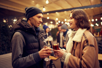 Happy couple in love in romantic dating with hot drinks, enjoying themselves, dressing warmly, looking at each other and smiling.