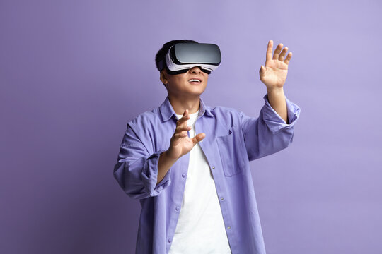 Focused Man Trying VR. Portrait of Amazed Asian Guy Discovering New Technologies Wearing Virtual Reality Headset, Futuristic 3d Vision. Indoor Studio Shot Isolated on Violet Background 