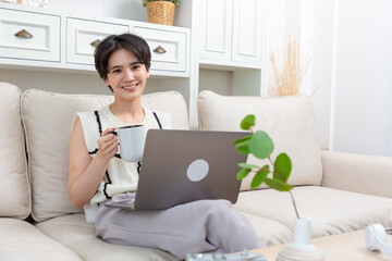 Relaxed asian woman freelancer female student browsing networks sitting on sofa looks at laptop screen.