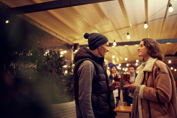 New acquaintances at Christmas holidays and parties. Happy man and girl at romantic dating with hot drinks. Concept of emotions, vacations, love, friendship