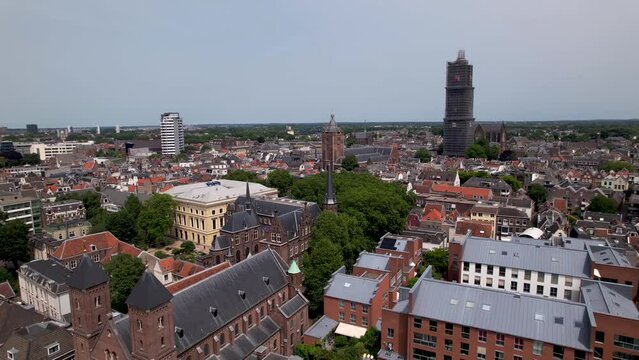 Upward movement aerial view of De Dom medieval cathedral tower in scaffolding in Dutch city center of Utrecht towering over the cityscape with rooftops of the historic town in the foreground